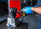 A man in a workshop wearing blue latex gloves pours compressor oil into an air compressor pump