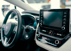 The cream and black interior of a car with the focus on the wheel, driver's area and especially the stereo system and central display.
