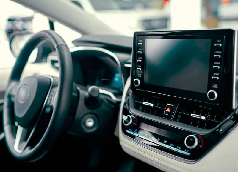 The cream and black interior of a car with the focus on the wheel, driver's area and especially the stereo system and central display.
