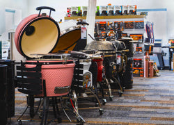 The interior of a grill store with a lineup of gas and pellet fueled smokers and grills and accessories and smoking fuel in the background