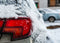 The right rear bumper and light of a grey 4-door Sedan covered with snow and ice on a snow covered street.